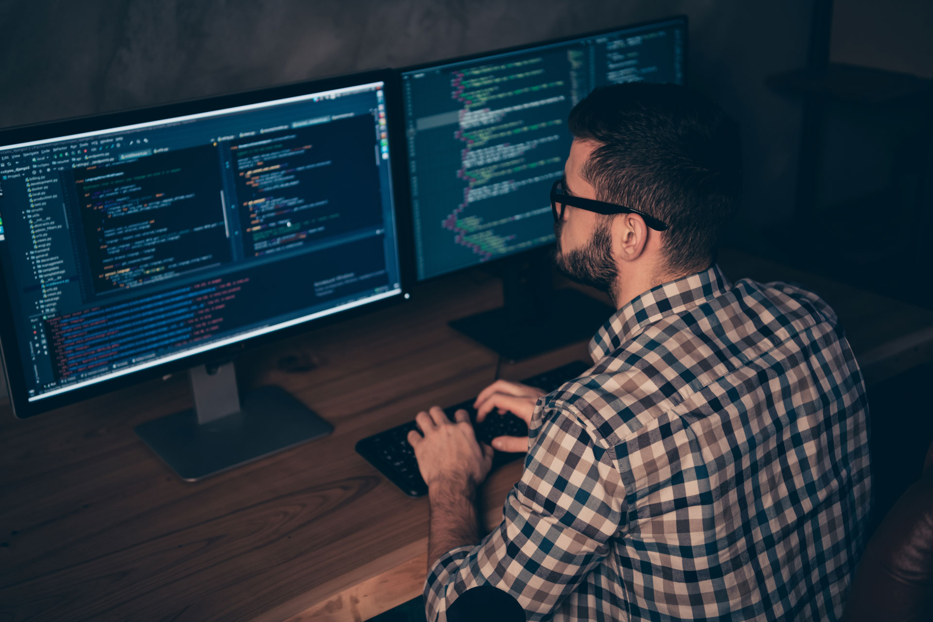 Mitarbeiter hinter 2 Monitoren mit Code-Editor