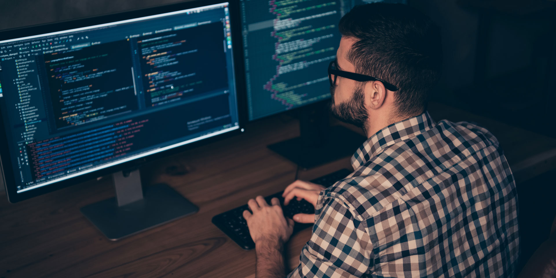 Mitarbeiter hinter 2 Monitoren mit Code-Editor